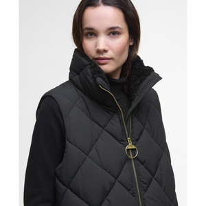 Kuvassa naisella on musta Barbour Bernice Puffer toppaliivi jossa on pehmeä teddyvuorattu kaulus ja näyttävä kullanvärinen vetoketju.