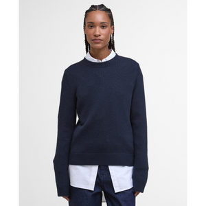 Kuvassa naisella on kauluspaidan päällä tummansininen Barbour Woodhouse villasekoiteneule.