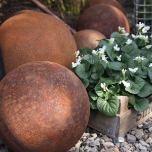 Kuvassa on eri kokoisia, ruosteisia koristepalloja jotka sopivat puutarhakoristeiksi.