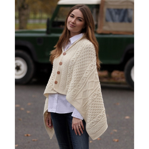 Kuvassa naisella on päällään merinovillainen, luonnonvalkoinen Walker Hawkesin neuleponcho jossa on ruskeat napit.