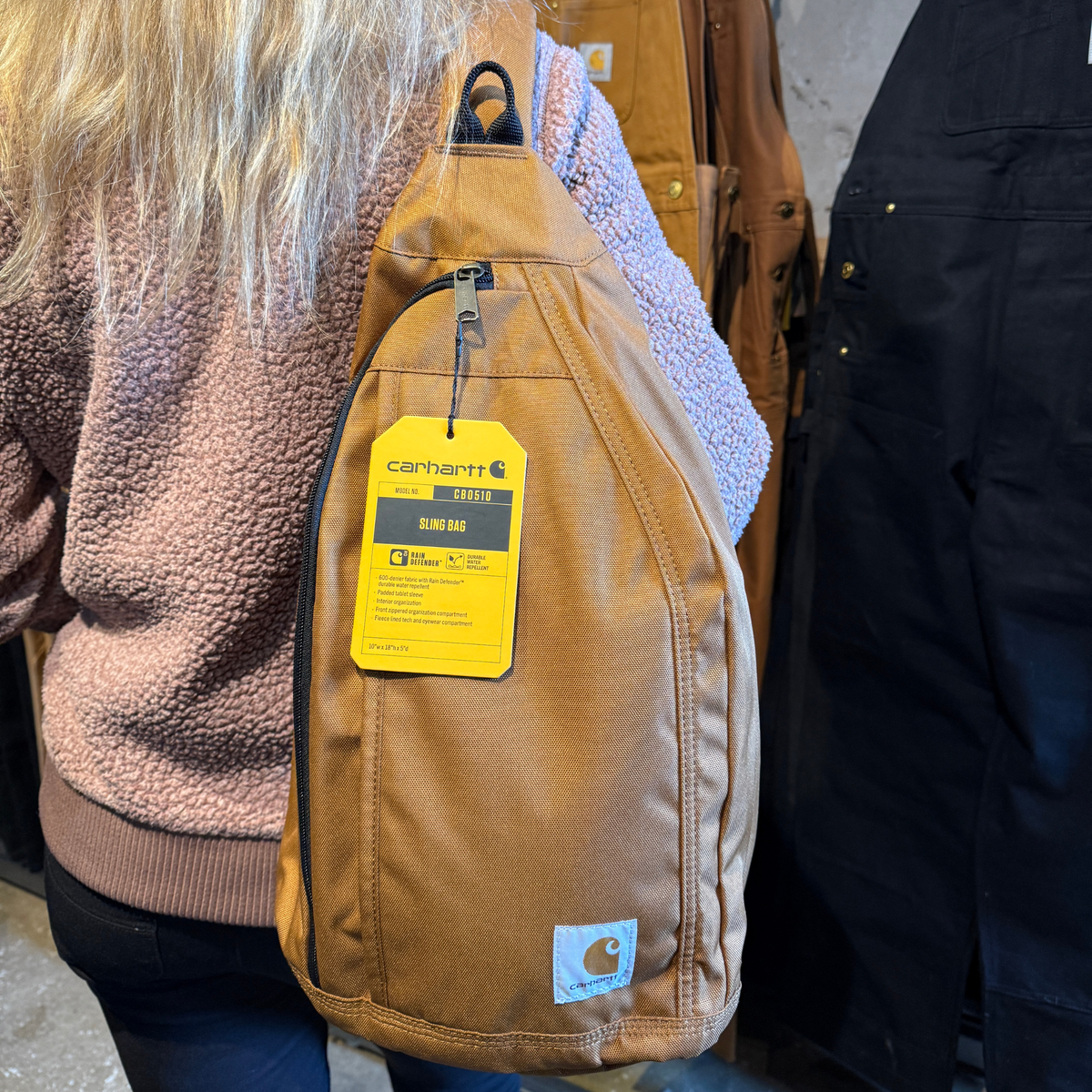 Ruskea tilava Carharttin olkalaukku naismallin olkapäällä.