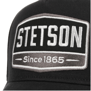 Stetson Trucker Cap 1865 -lippiksen etumerkki lähikuvassa, valkoinen Stetson-teksti ja harmaa Since 1865 -kirjailu.