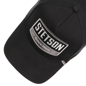 Stetson Trucker Cap 1865 musta lippis yläviistosta, kirjailtu logomerkki ja lipan raidallinen yksityiskohta.