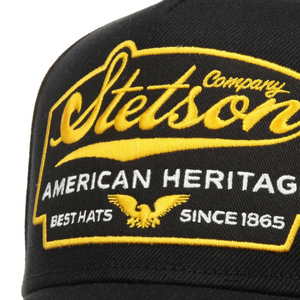 Stetson Trucker Cap Eagle -lippiksen etukirjailu lähikuvassa, keltainen Stetson-logo, kotka ja valkoinen American Heritage -teksti.