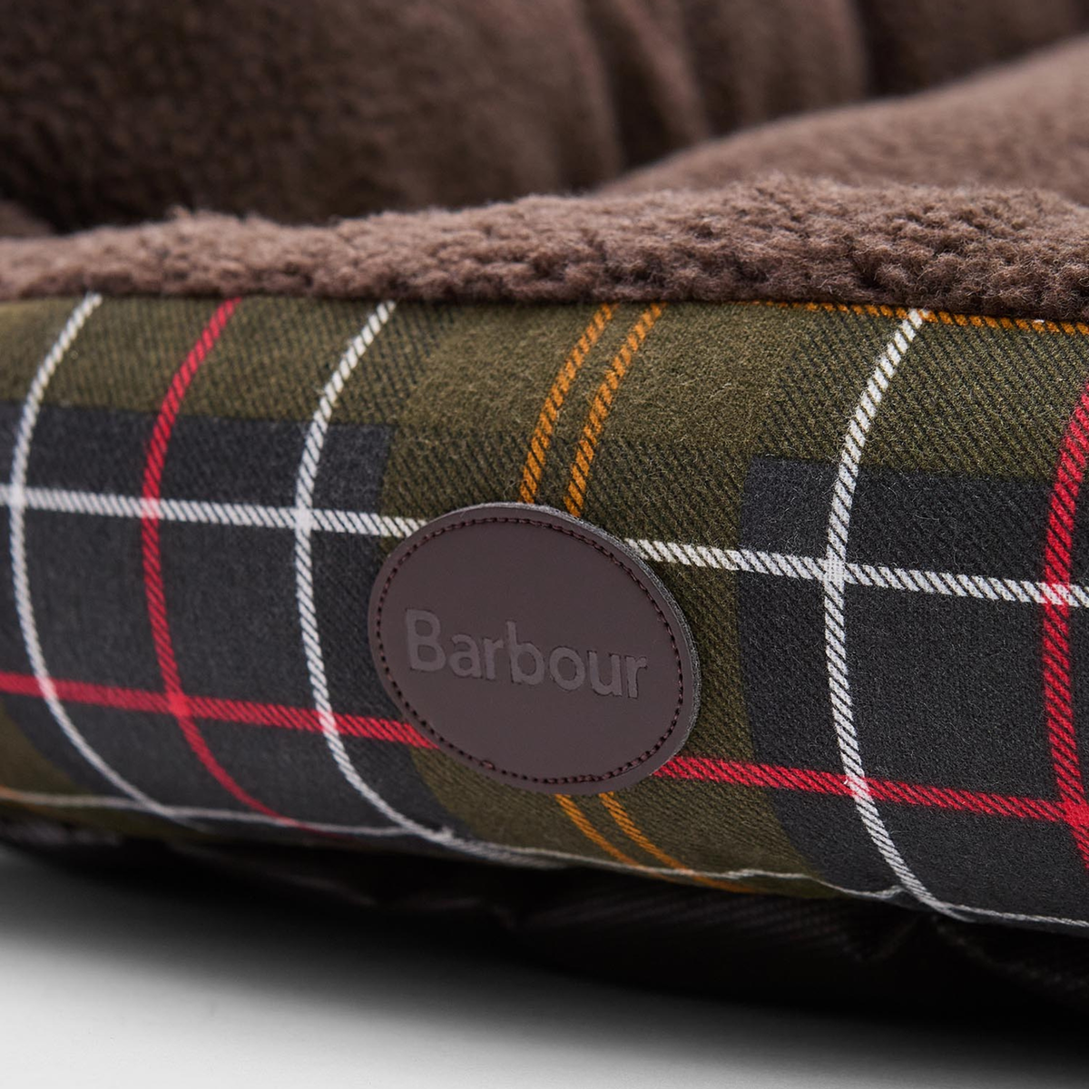 Kuvassa on Barbourin pehmeä koiranpeti jonka reunassa on nahkainen Barbour -logolaatta.