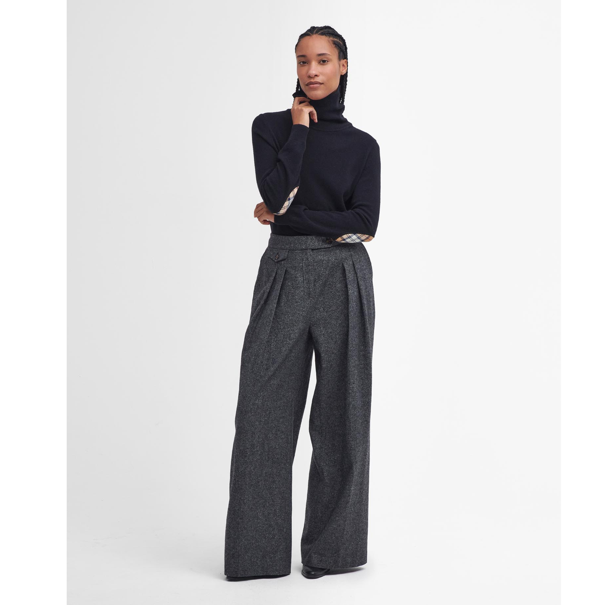 Kuvassa naisen päällä on musta Barbour pooloneule jossa on tartan-kuosiset kyynärpaikat.