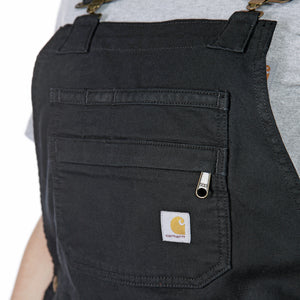 Lähikuvassa mustat Carhartt naisten lappuhaalarishortsit joiden etuosassa on tasku sekä Carhartt logo. 