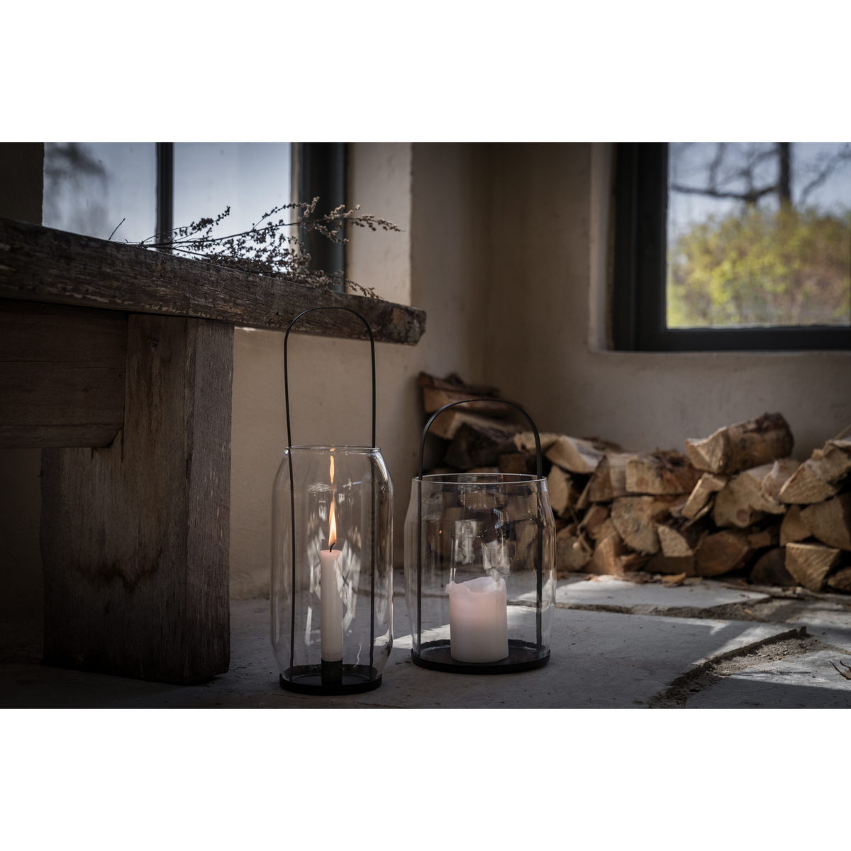 Lyhdyssä on musta metallinen kynttilänalunen ja kahva sekä lasisylinteri jonka sisälle kynttilä laitetaan.