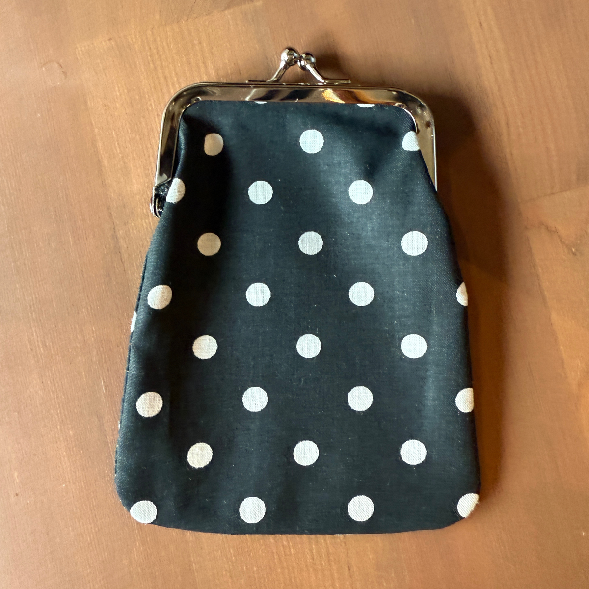 Kuvassa on musta kangaskukkaro jossa on valkoisia pilkkuja.