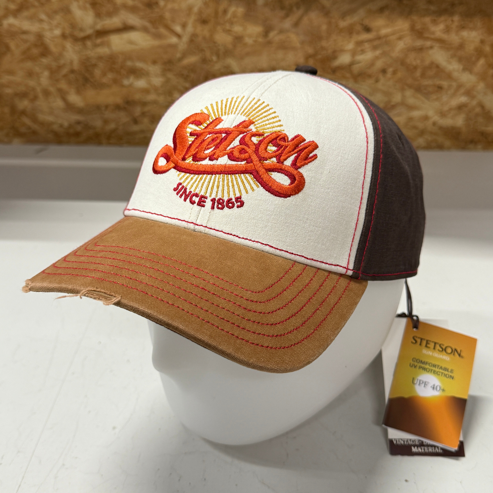 Kuvan Stetson -lippis on käsitelty kuluneen näköiseksi. Siinä on ruskea lippa ja takaosa ja valkoinen etuosa jossa oranssi Stetson -teksti.
