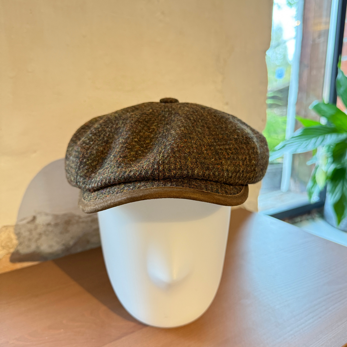 Kaarevassa lipassa on ruskea koristenauha reunassa ja hatun keskellä on koristenappi.