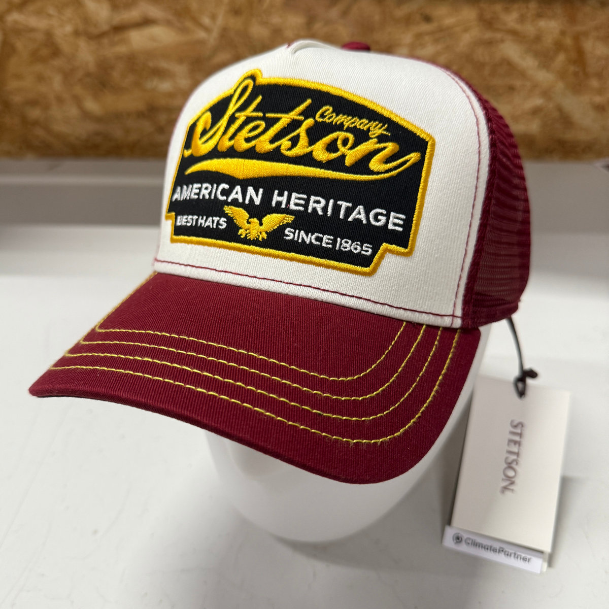 Kuvassa Stetson Trucker Cap jossa tummanpunainen verkko-osa takana, tummanpunainen lippa ja valkoinen etuosa jossa kelta-musta American Heritage brodeeraus.