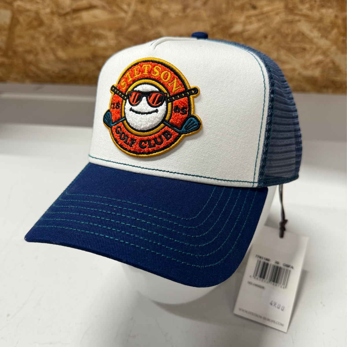 Kuvassa on sinivalkoinen Stetson Trucker Cap -lippis jossa on etuosassa golf -aiheinen kuva.