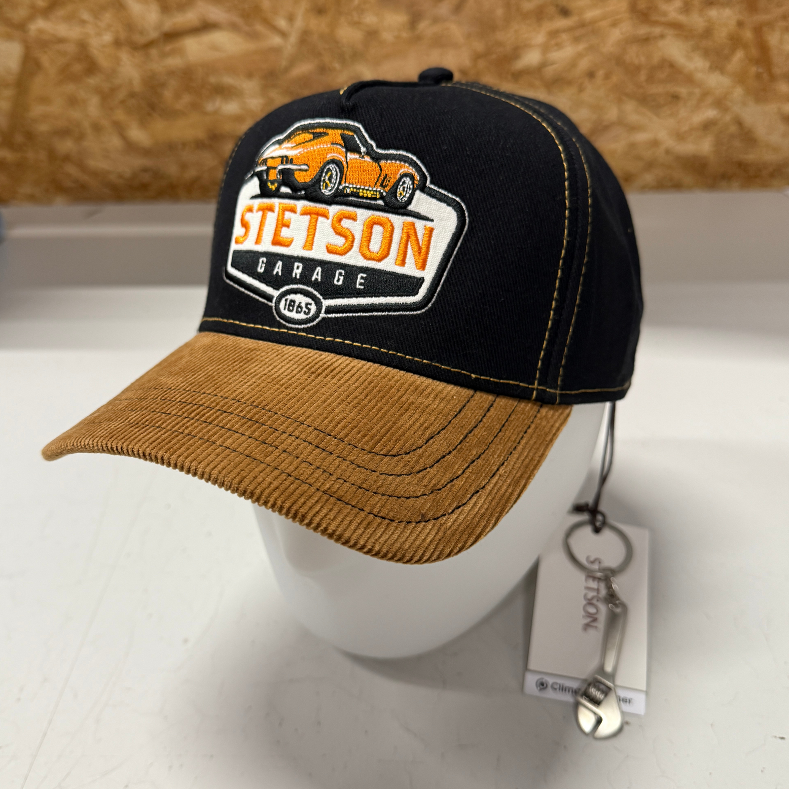 Kuvassa on musta Stetson Garage -sarjan lippis jossa kullanruskea lippa, autoaihe sekä mukana tuleva minikokoinen jakoavain.