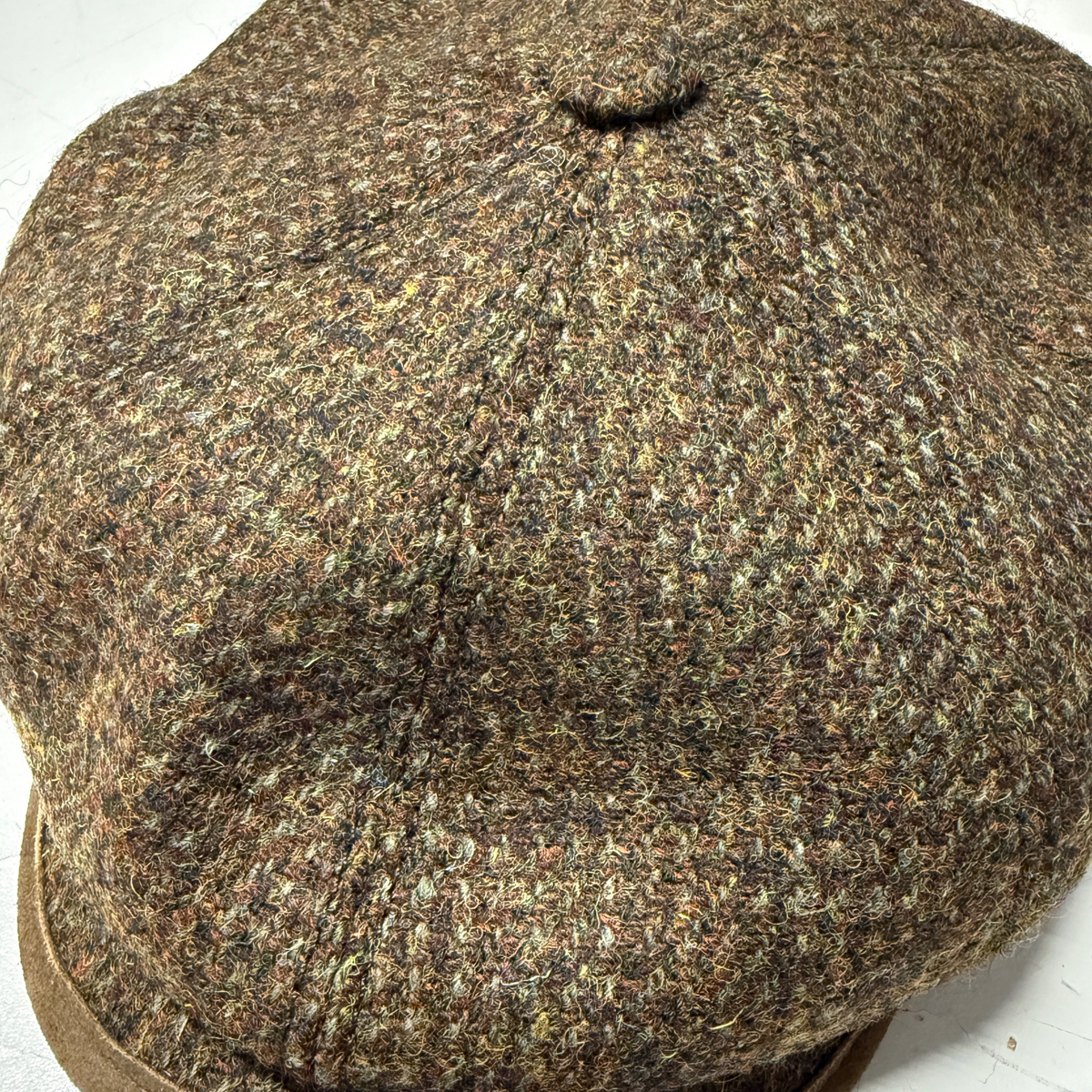 Tämä Stetsonin Flat Cap on valmistettu vihreän ja ruskean sävyisestä Harris Tweed -kankaasta ja sen keskellä on nappi.