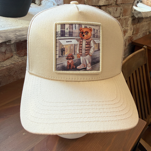 Kuvassa on beige Baron filou lippis jossa Filou nalle ulkoiluttaa koiraansa kadulla. 