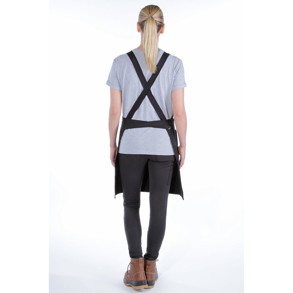 Kuvassa on Carharttin musta Duck Canvas esiliina takaa päin kuvattuna naisen päällä valkoisella pohjalla.