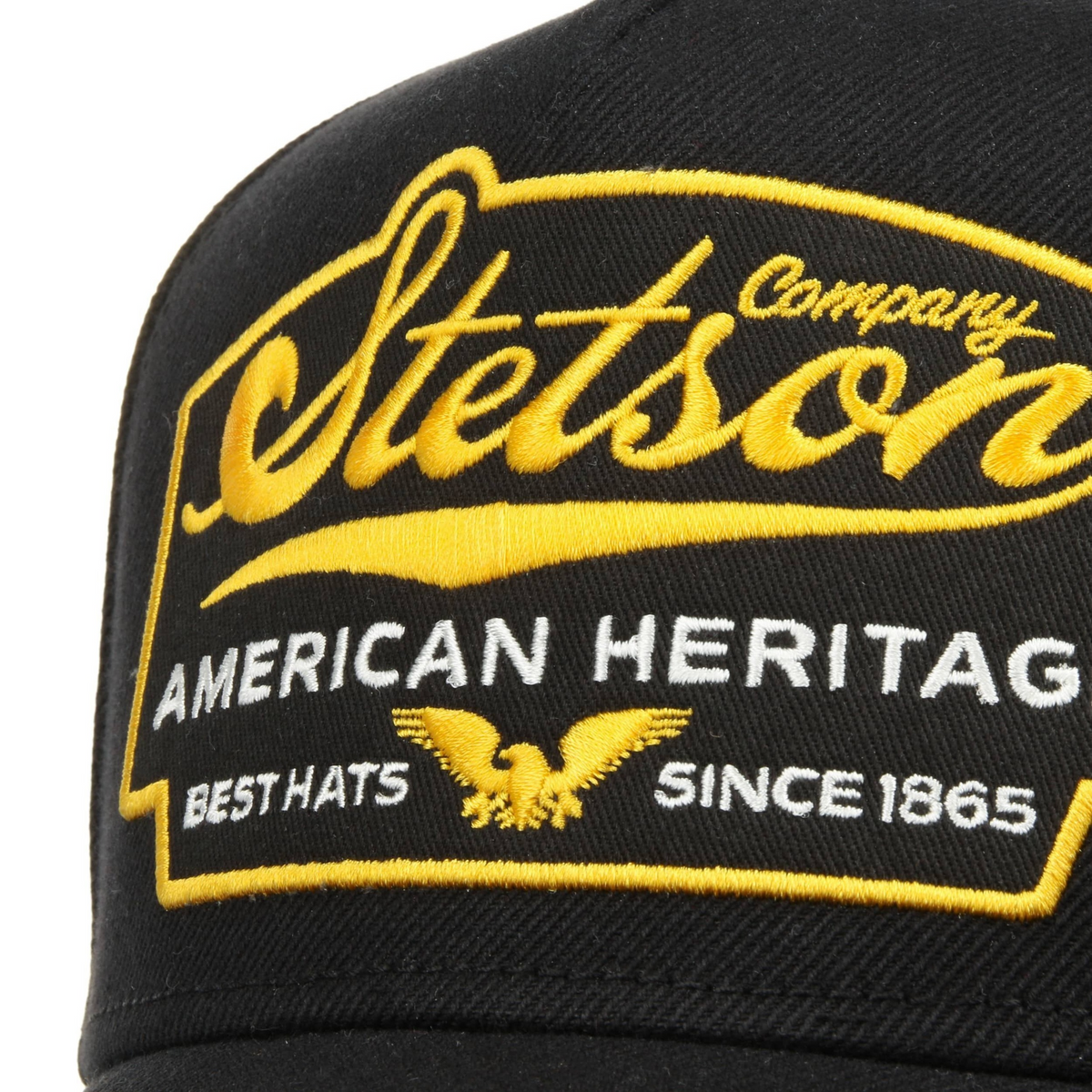 Stetson Trucker Cap Eagle -lippiksen etukirjailu lähikuvassa, keltainen Stetson-logo, kotka ja valkoinen American Heritage -teksti.