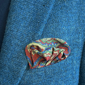 Wellington of Bilmore monivärinen silkkitaskuhuivi sinisen tweedbleiserin rintataskussa, pyöreästi laskostettuna.